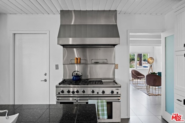 kitchen with light tile patterned floors, wall chimney exhaust hood, wood ceiling, and stainless steel stove