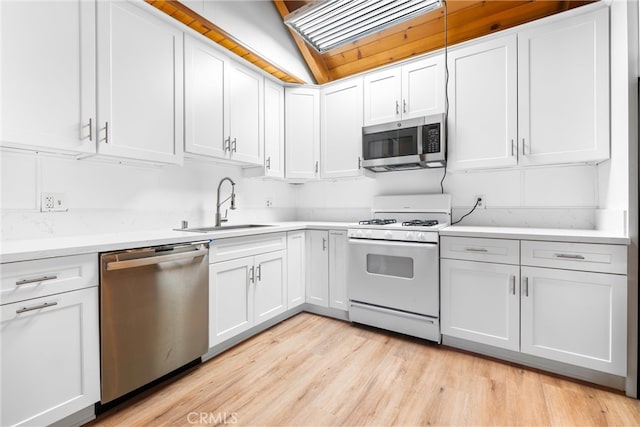 kitchen with white cabinets, sink, appliances with stainless steel finishes, light wood-type flooring, and vaulted ceiling