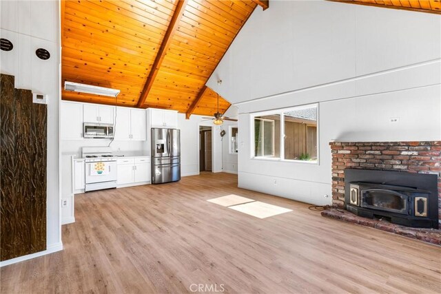 unfurnished living room featuring beamed ceiling, light wood-type flooring, a wood stove, and wooden ceiling