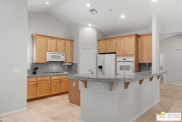 kitchen with kitchen peninsula, white appliances, light brown cabinetry, a kitchen bar, and decorative backsplash