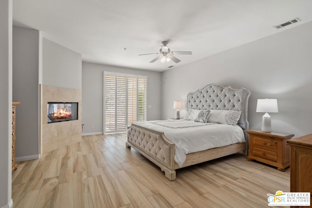 bedroom with light wood-type flooring, a tile fireplace, and ceiling fan