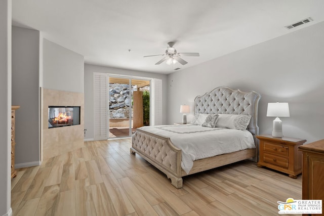 bedroom featuring access to outside, a fireplace, light hardwood / wood-style floors, and ceiling fan