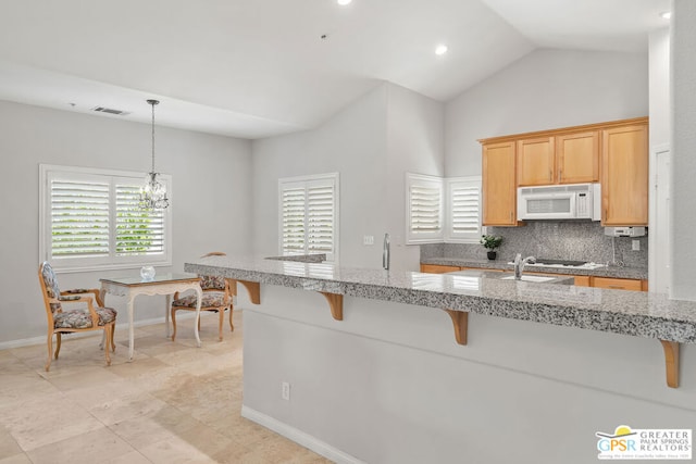 kitchen with a kitchen breakfast bar, hanging light fixtures, backsplash, white appliances, and a notable chandelier