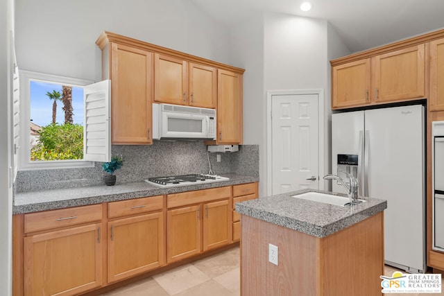 kitchen featuring white appliances, a center island with sink, sink, and backsplash