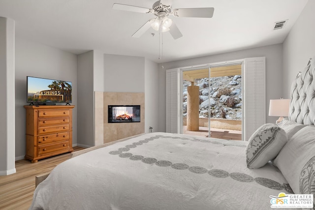 bedroom featuring access to outside, light hardwood / wood-style floors, a multi sided fireplace, and ceiling fan