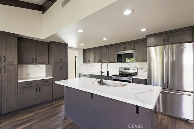 kitchen featuring sink, backsplash, stainless steel appliances, an island with sink, and dark hardwood / wood-style flooring