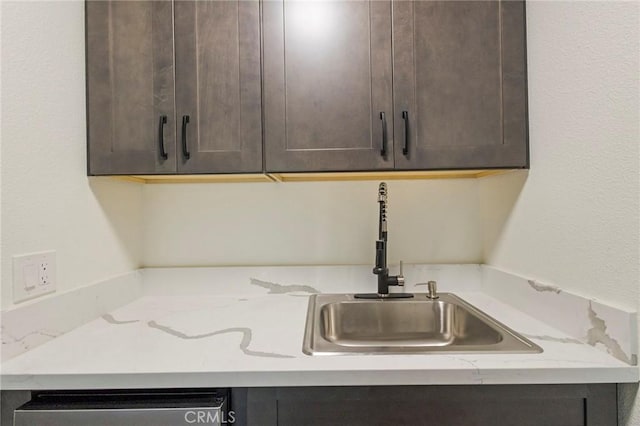 kitchen featuring dishwasher, light stone countertops, sink, and dark brown cabinetry