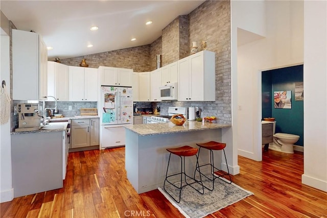 kitchen featuring tasteful backsplash, white cabinets, a kitchen breakfast bar, light hardwood / wood-style floors, and white appliances