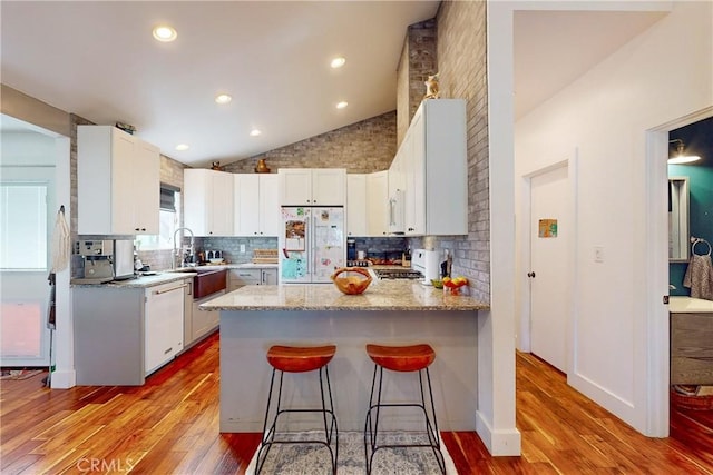 kitchen with lofted ceiling, refrigerator, white dishwasher, kitchen peninsula, and white cabinets