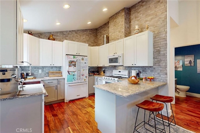 kitchen with a breakfast bar, white cabinetry, light hardwood / wood-style floors, kitchen peninsula, and white appliances