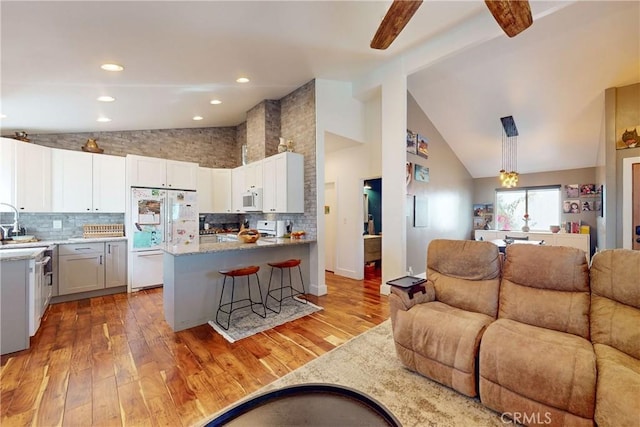 kitchen with pendant lighting, white appliances, white cabinetry, a kitchen breakfast bar, and light wood-type flooring