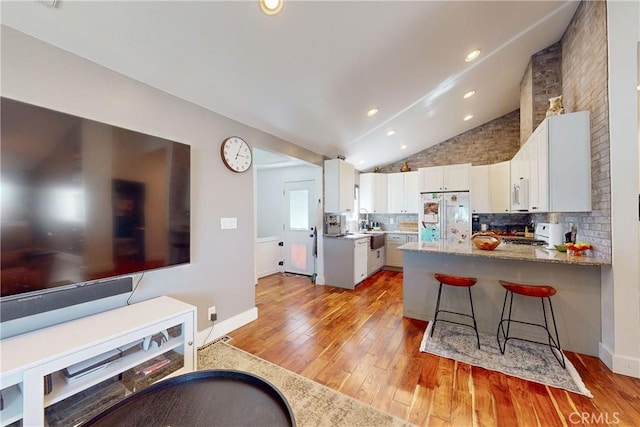 kitchen featuring vaulted ceiling, kitchen peninsula, white fridge, light stone countertops, and white cabinets