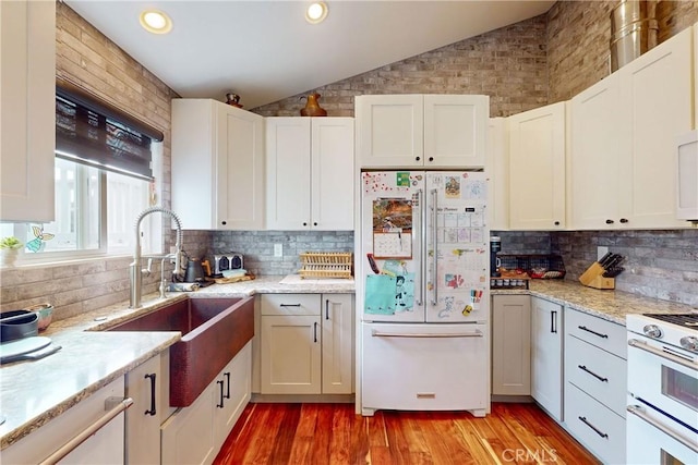 kitchen featuring sink, white appliances, white cabinets, vaulted ceiling, and light wood-type flooring