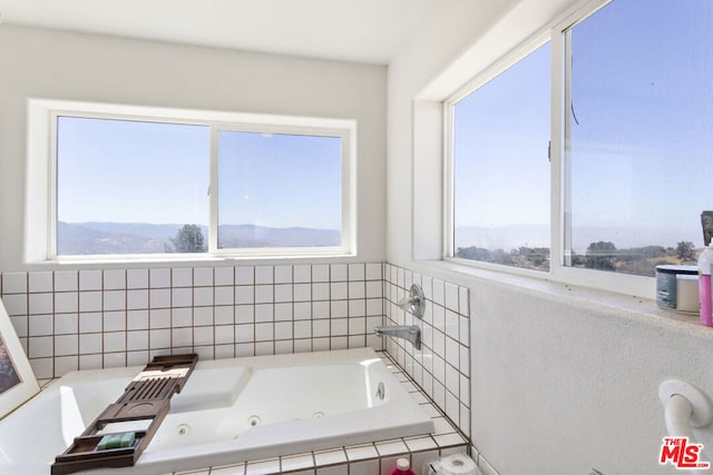 bathroom featuring a mountain view, tiled bath, and a healthy amount of sunlight