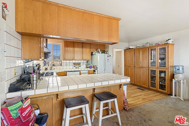 kitchen featuring kitchen peninsula, white appliances, tile countertops, a breakfast bar, and light wood-type flooring