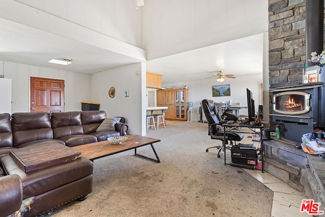 carpeted living room featuring a wood stove and ceiling fan