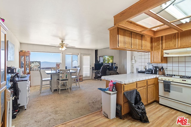 kitchen with light hardwood / wood-style floors, white gas range oven, tile counters, kitchen peninsula, and a skylight