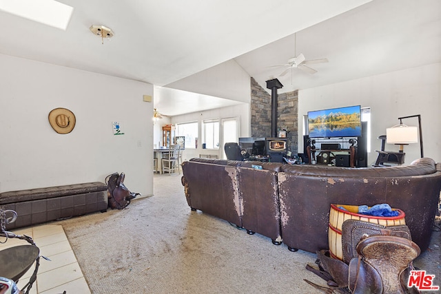 living room featuring ceiling fan, lofted ceiling with skylight, and a wood stove