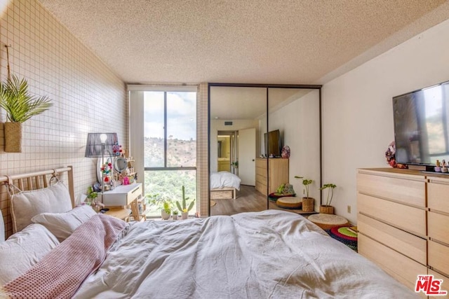 bedroom with a textured ceiling, wood-type flooring, a wall of windows, and tile walls