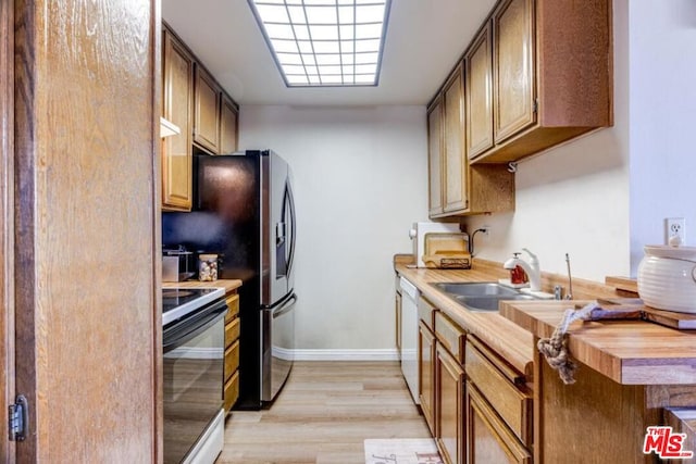 kitchen with stainless steel appliances, butcher block counters, sink, and light hardwood / wood-style flooring