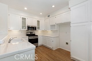 kitchen featuring sink, white cabinetry, appliances with stainless steel finishes, tile counters, and light wood-type flooring