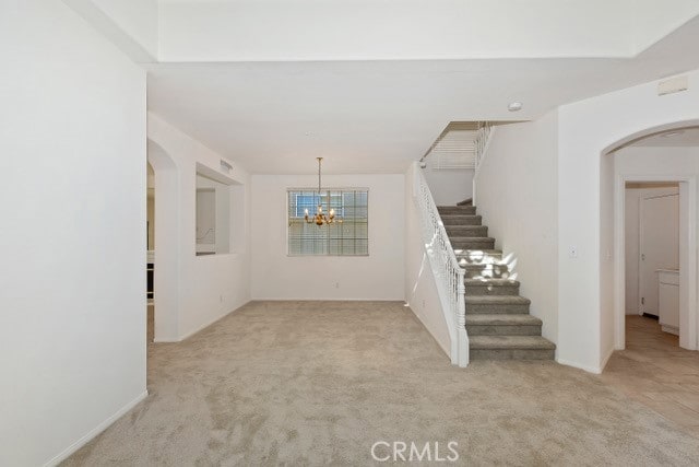 empty room with light carpet and a notable chandelier