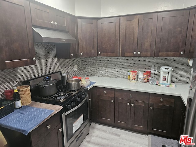 kitchen featuring light hardwood / wood-style floors, dark brown cabinetry, wall chimney exhaust hood, and stainless steel gas range