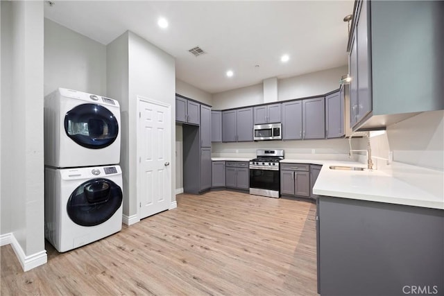 kitchen with gray cabinetry, sink, stainless steel appliances, stacked washer and dryer, and light wood-type flooring