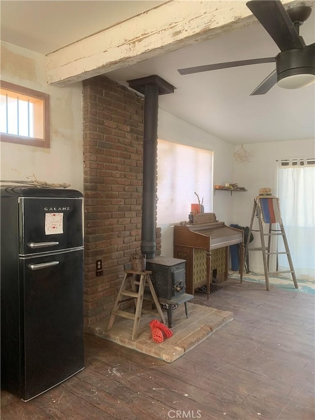 interior space featuring a wood stove, black refrigerator, vaulted ceiling with beams, dark hardwood / wood-style floors, and ceiling fan