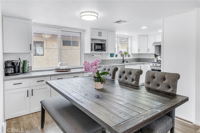 kitchen featuring black microwave, under cabinet range hood, visible vents, white cabinets, and stainless steel range with gas cooktop