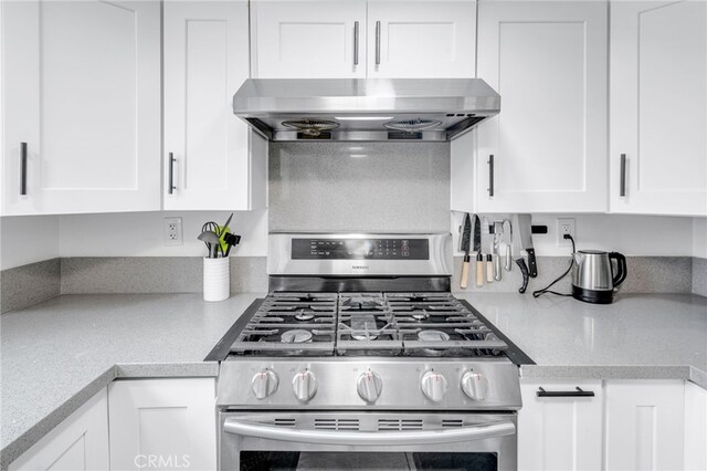 kitchen with wall chimney exhaust hood, white cabinetry, light countertops, and gas stove