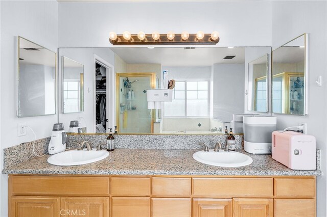 full bathroom featuring double vanity, a sink, a walk in closet, and a shower stall