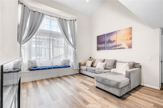 living room featuring lofted ceiling, light wood-style flooring, and baseboards