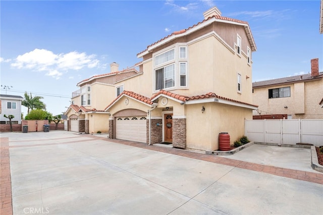 mediterranean / spanish-style home featuring concrete driveway, a tile roof, fence, and stucco siding