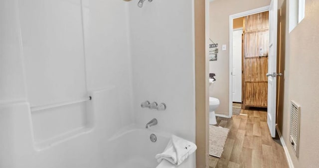 bathroom featuring washtub / shower combination, toilet, and hardwood / wood-style flooring