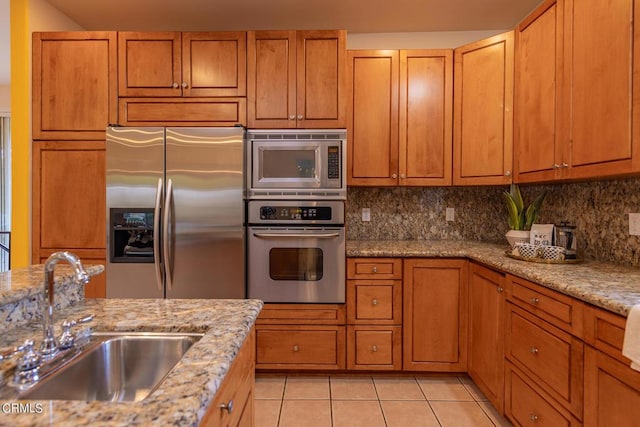 kitchen featuring light stone counters, sink, light tile patterned floors, and stainless steel appliances