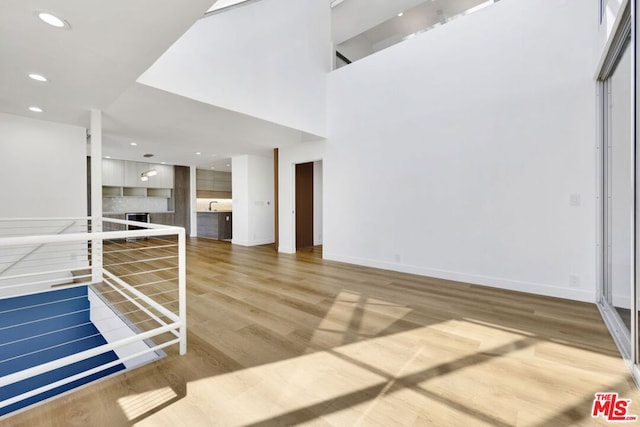 unfurnished living room with wood-type flooring, a high ceiling, and sink