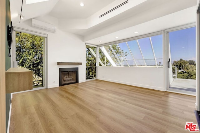 unfurnished living room featuring a skylight, light hardwood / wood-style flooring, and a wall unit AC