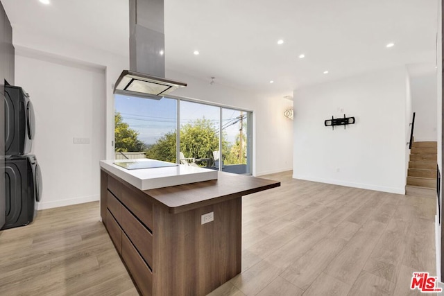 kitchen featuring island exhaust hood, light hardwood / wood-style floors, stacked washer / drying machine, and a kitchen island