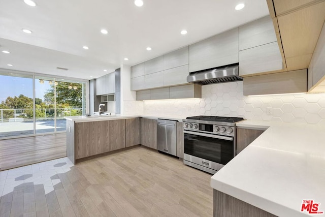 kitchen featuring light hardwood / wood-style floors, kitchen peninsula, backsplash, exhaust hood, and appliances with stainless steel finishes