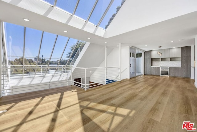 unfurnished living room featuring a high ceiling, light hardwood / wood-style floors, beverage cooler, and a healthy amount of sunlight