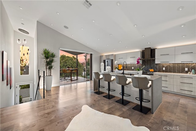 kitchen featuring a kitchen breakfast bar, hardwood / wood-style floors, high vaulted ceiling, and a kitchen island with sink