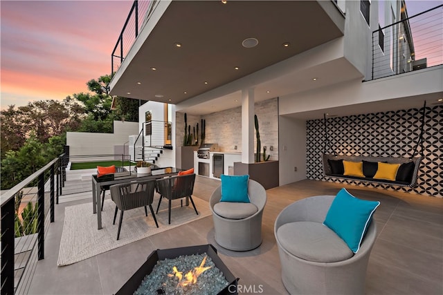 patio terrace at dusk featuring a balcony and an outdoor fire pit