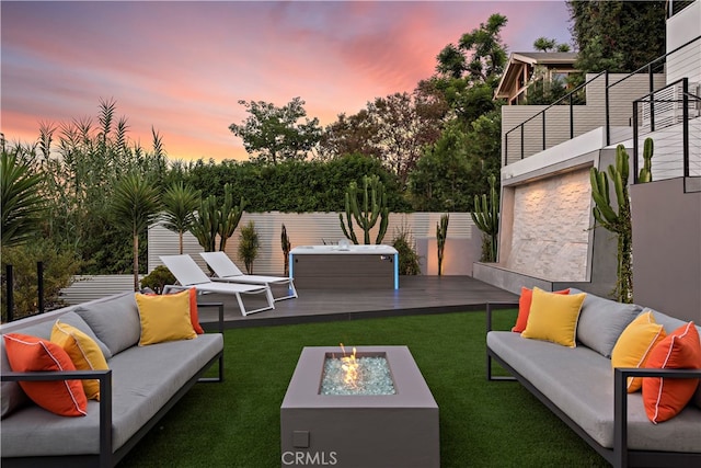 patio terrace at dusk featuring an outdoor living space with a fire pit, a wooden deck, and a lawn