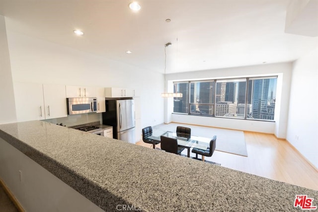 kitchen featuring appliances with stainless steel finishes, light hardwood / wood-style floors, white cabinetry, and pendant lighting