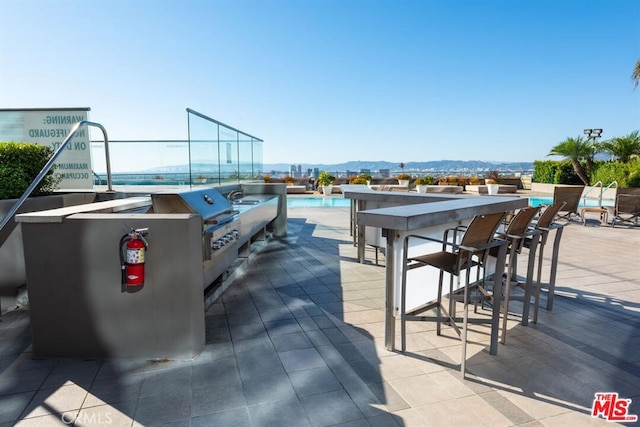 view of patio / terrace with a community pool, a mountain view, an outdoor bar, and a grill