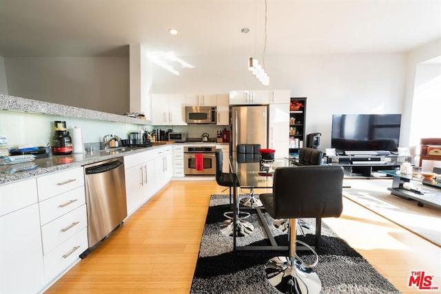 kitchen featuring white cabinetry, pendant lighting, stainless steel appliances, and light hardwood / wood-style flooring