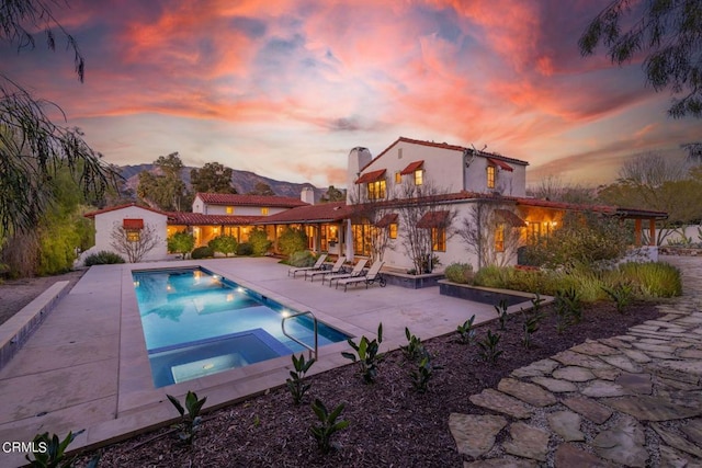 pool at dusk featuring a patio, a mountain view, and an in ground hot tub