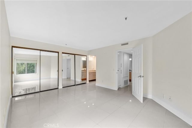 unfurnished bedroom featuring light tile patterned flooring, connected bathroom, and two closets