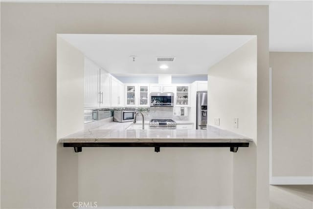 260 Cagney Ln Unit 105, Newport Beach, CA 92663 - kitchen with stainless steel appliances, a peninsula, glass insert cabinets, and white cabinetry
